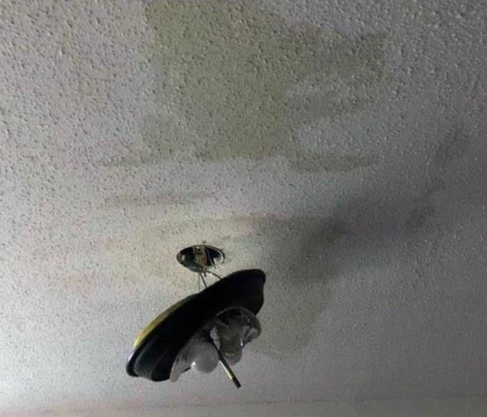 water stained drywall ceiling with light fixture hanging from it