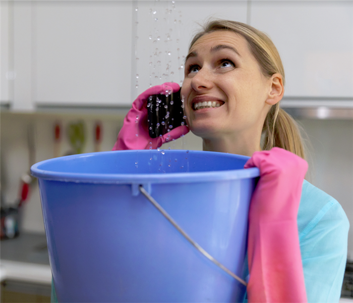 a woman holding a bucket to catch water falling from her ceiling